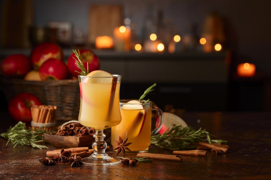 Glasses of mulled cider with apples and spices with candles in background