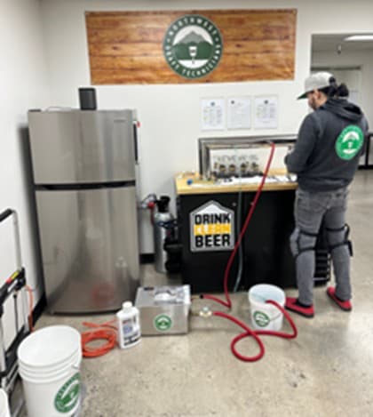 Technician cleaning beer tap lines in backroom with fridge in background
